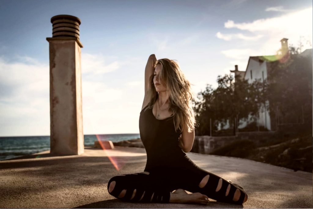 Yogateacher Dela Marlen in sitzender Pose mit hinter dem Rücken verschränkten Händen